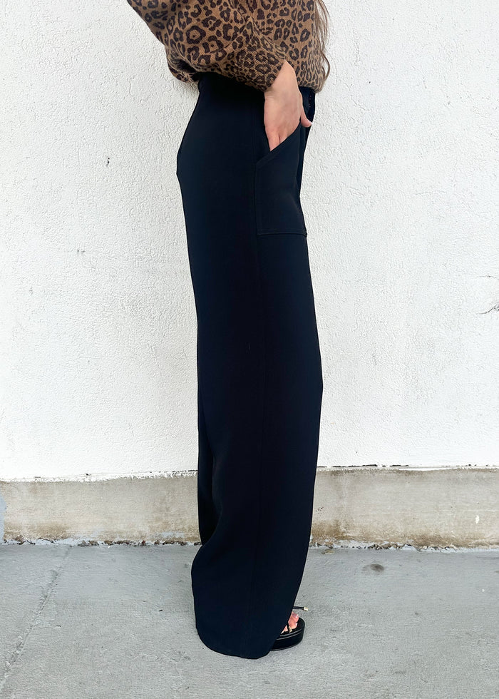 Person wearing black pants with a leopard print top against a white wall.