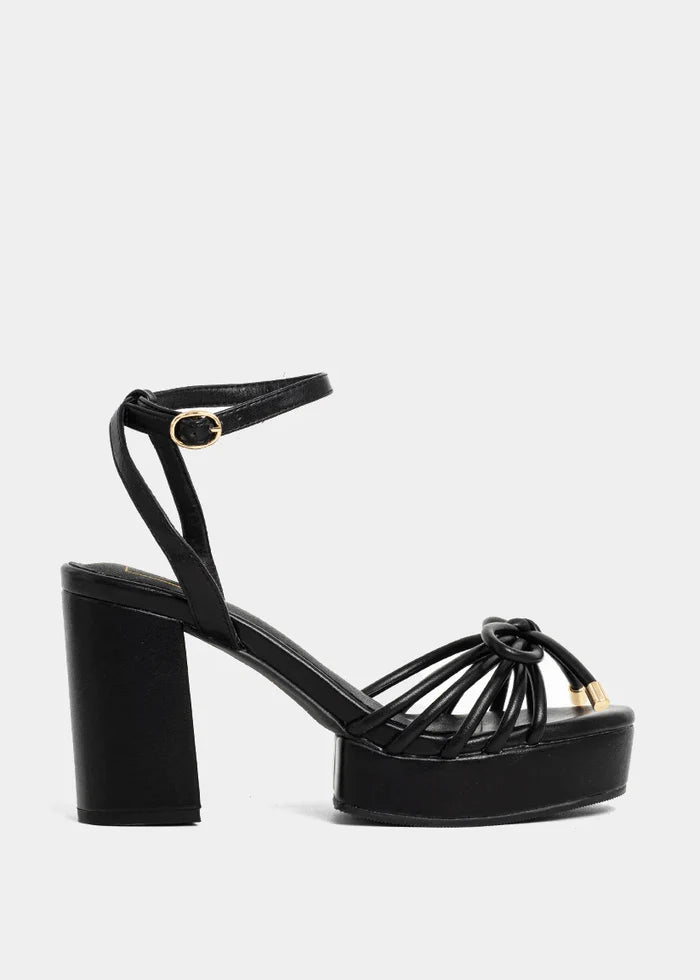 Black platform heels with strappy knotted vamp, chunky block heel, and adjustable ankle strap with buckle closure.