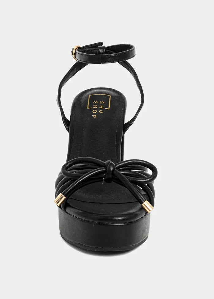 Black leather platform heel with knotted bow detail and ankle strap with gold hardware.