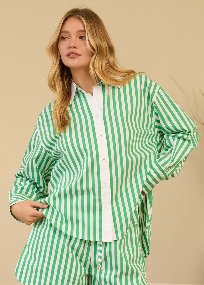 Woman wearing a green and white striped outfit standing in a room with a vase and plant in the background.