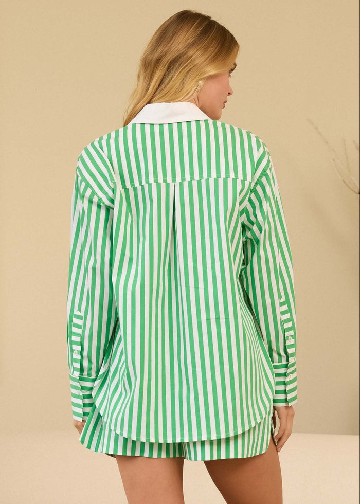 Woman wearing a green and white striped shirt and shorts in a room with a beige sofa and decorative plant.
