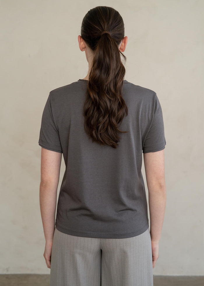 Woman wearing a charcoal gray short-sleeve t-shirt with raw edges, shown from behind.