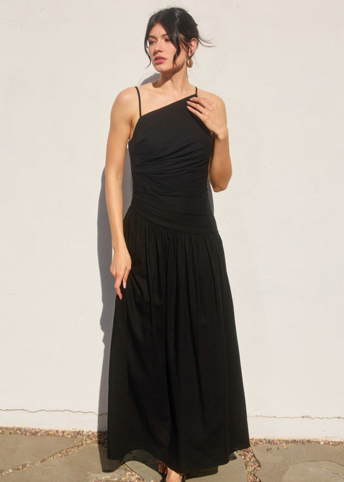 Black maxi dress with asymmetrical neckline, thin straps, ruched bodice, and drop waist with gathered skirt.