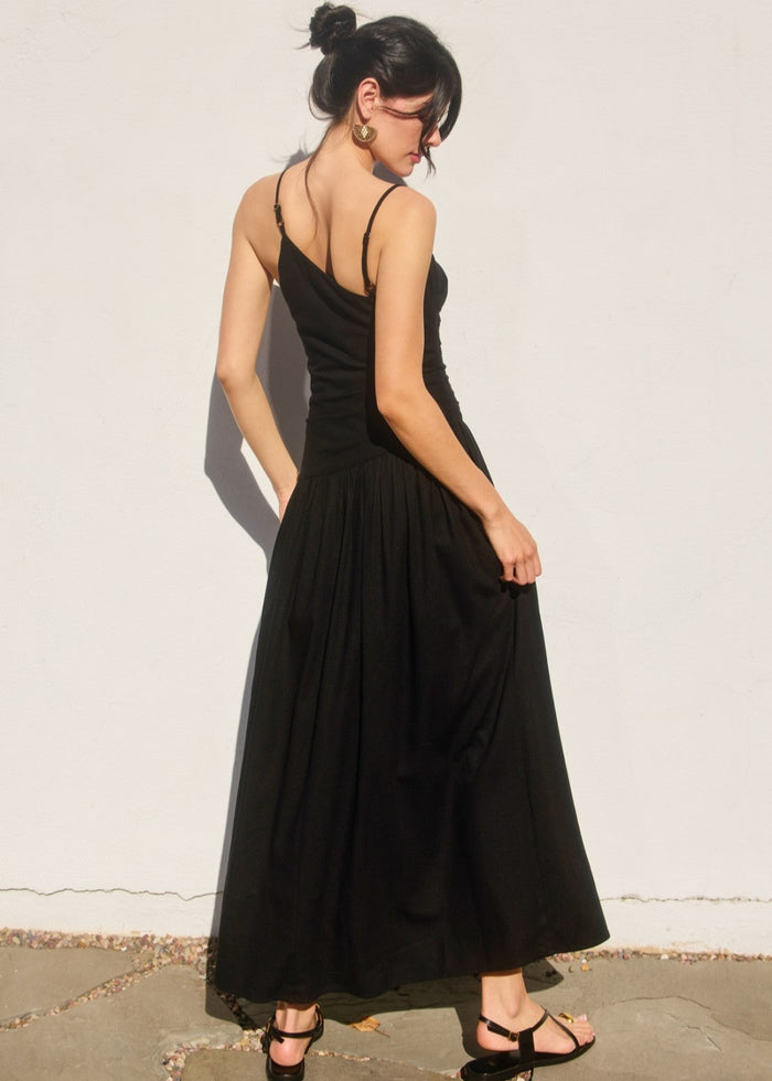 Black sleeveless maxi dress with drop waist, ruched detailing, and open back on model shown from behind.