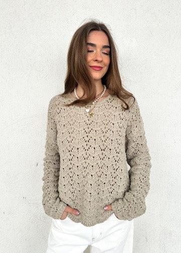 Cream knit sweater with textured chevron pattern and long sleeves worn with white pants.