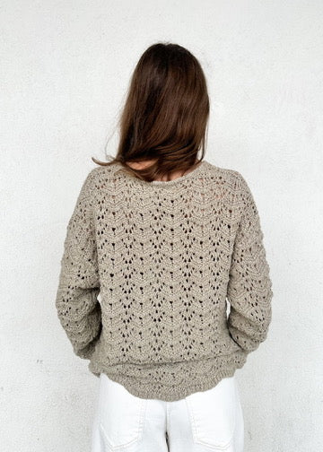 Beige knit sweater with open chevron pattern worn by model with long brown hair, shown from back view.
