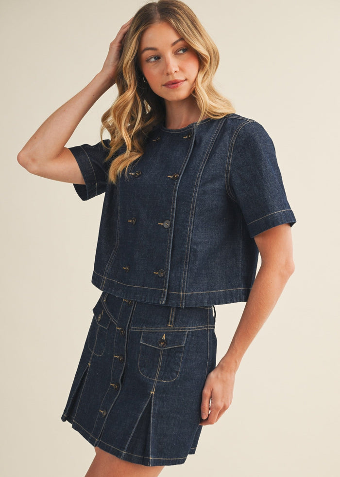 Woman wearing a denim outfit with a jacket and skirt on a beige background