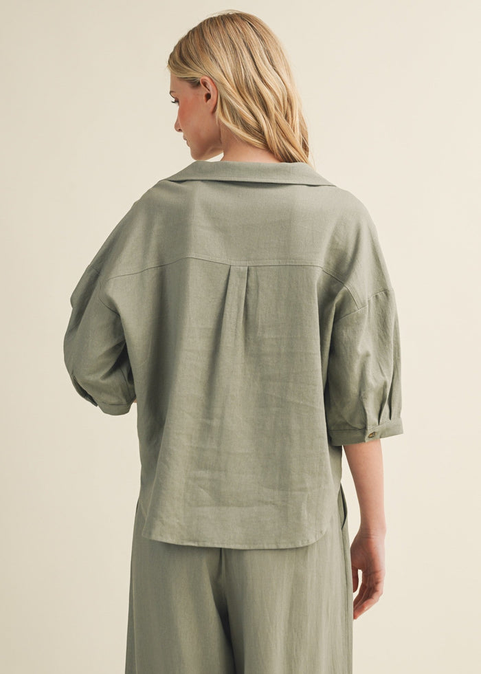 Sage green linen button-up top with three-quarter sleeves and collar, shown on model from back view.