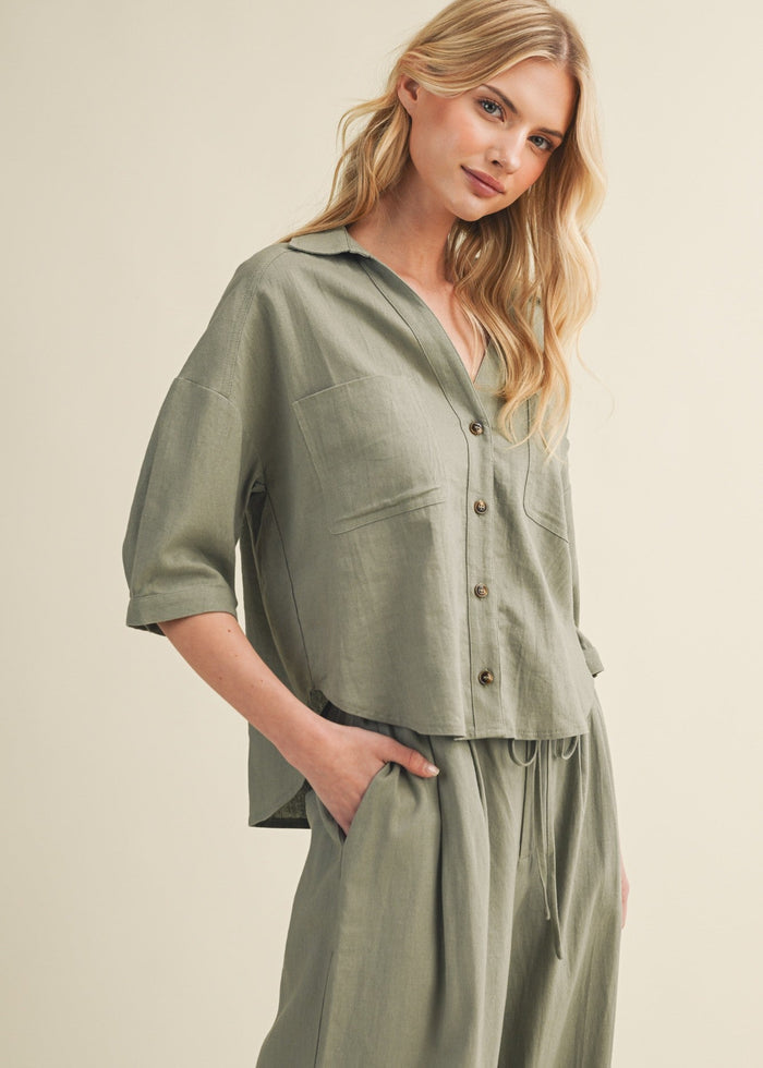 Sage green button-up top with three-quarter sleeves, collar, and front chest pockets on a model.