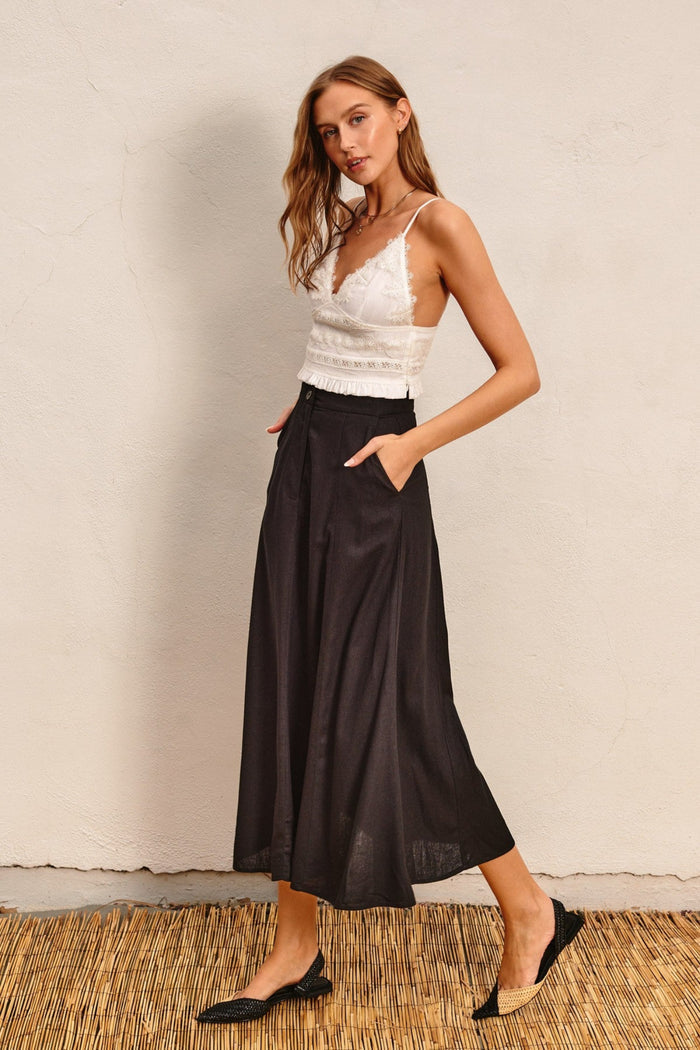 Black flared maxi skirt with high waist and side pockets, paired with white lace crop top.