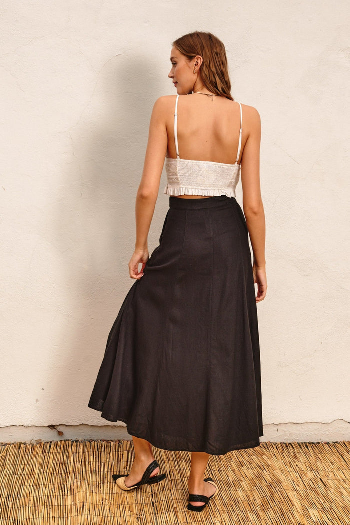 Black linen flared maxi skirt with high waist, shown from back on model wearing white crop top.