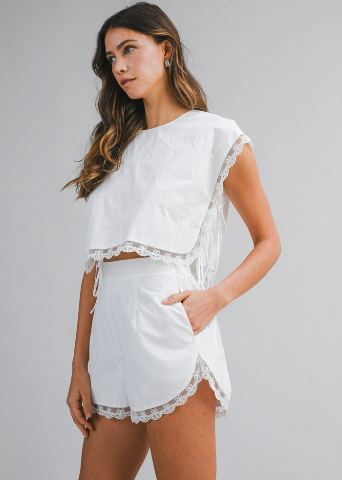 White high-waist shorts with lace trim hem and side pockets, paired with matching cropped lace-trimmed top.