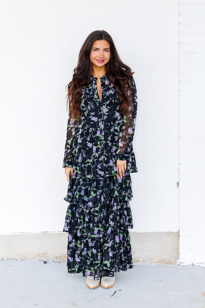 Black maxi dress with purple and green floral print, long sheer sleeves, and tiered ruffle skirt.