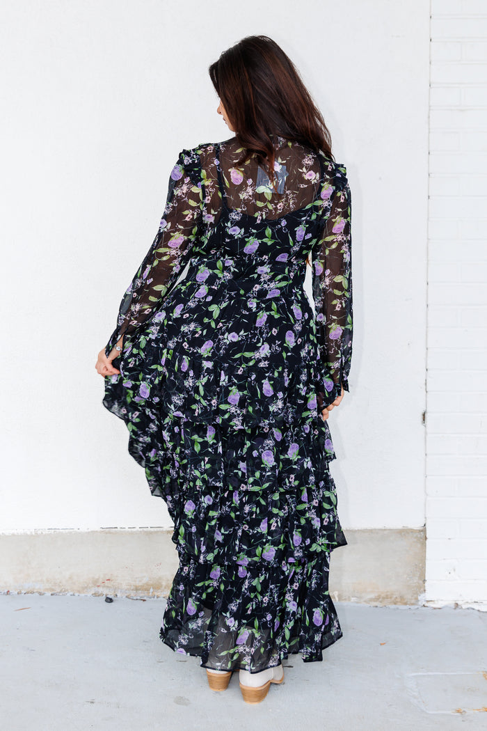Black maxi dress with purple and white floral print, long sleeves, and tiered ruffle skirt, shown from back view.