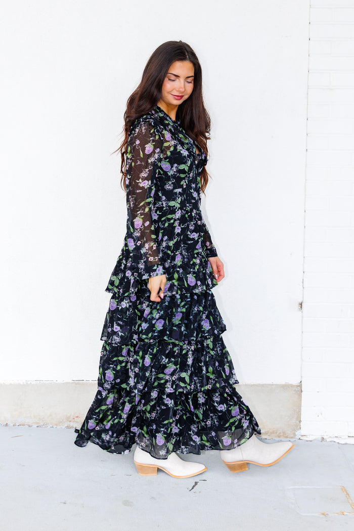 Black maxi dress with purple and green floral print, tiered ruffled skirt, and long sleeves.