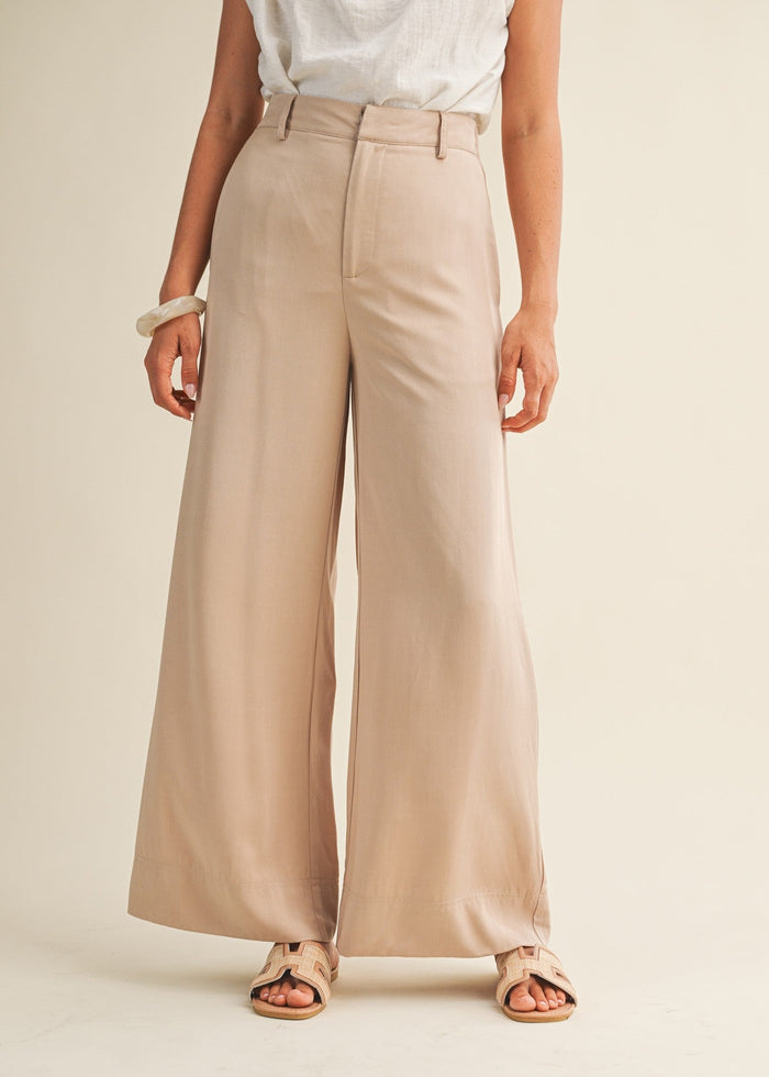 Beige wide-leg pants with high waist and front zip closure worn with white sleeveless top.