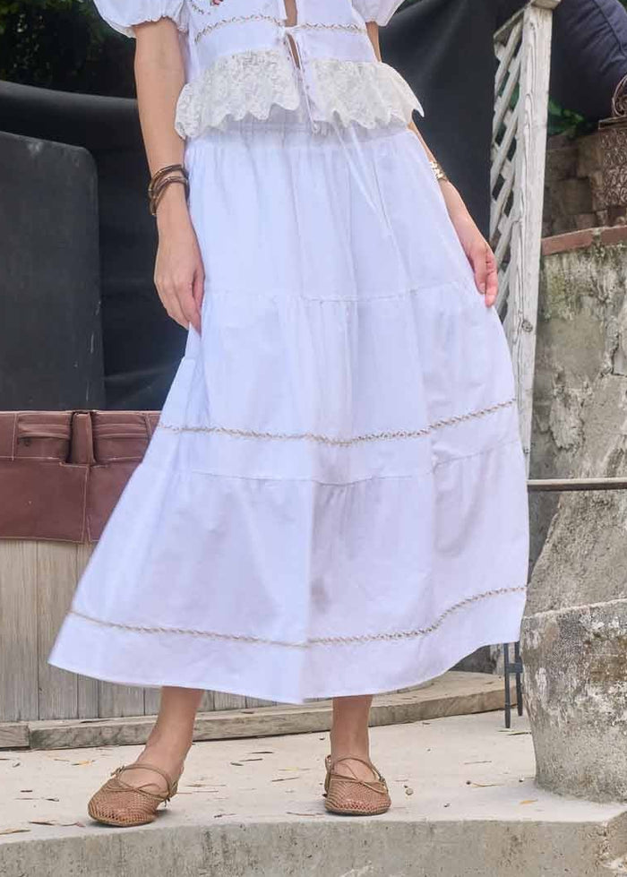 Light lavender midi skirt with tiered panels and tan embroidered trim details.
