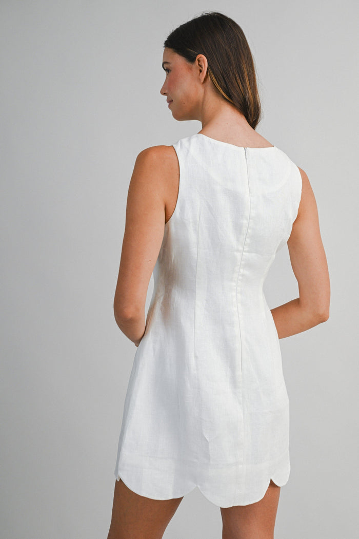 White linen sleeveless mini dress with a curved hem, shown from the back on a model.