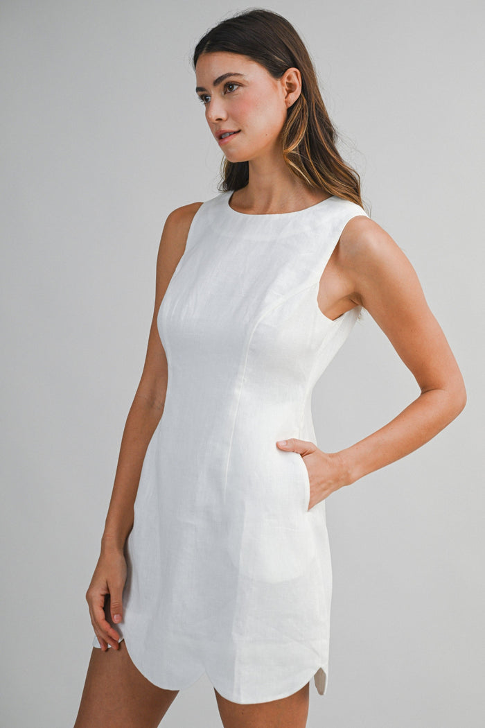 White sleeveless linen mini dress with crew neckline and side pocket detail on model.