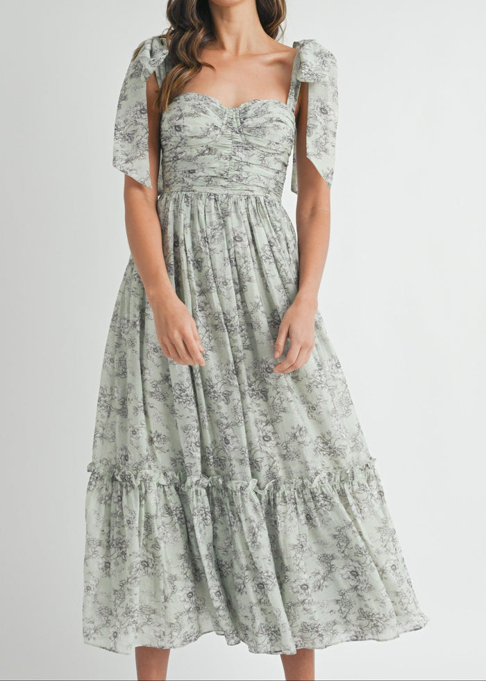 Sage green midi dress with gray floral print, sweetheart neckline, ruched bodice, puff sleeves, and tiered skirt.