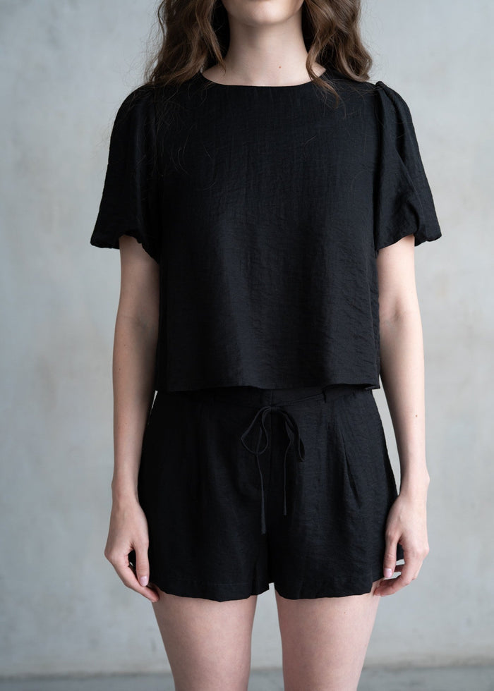 Black short-sleeved t-shirt with gathered puff sleeves and crew neckline on model.