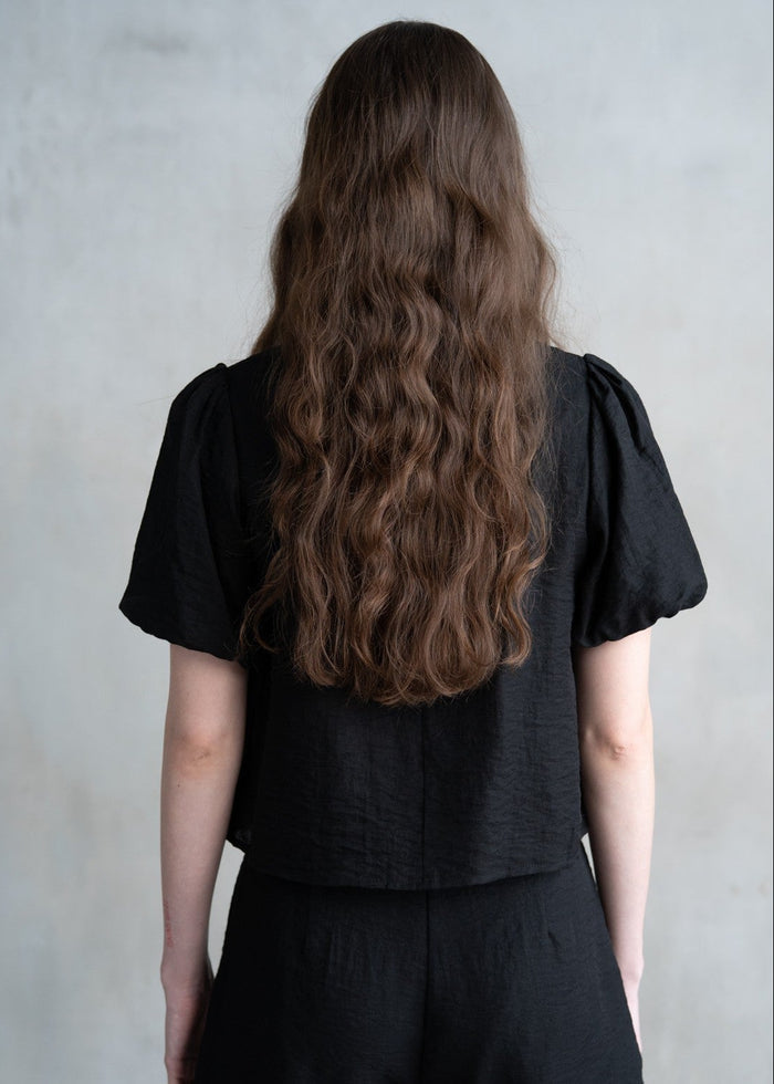 Black t-shirt with short puffed sleeves, shown from back on model with long brown hair.