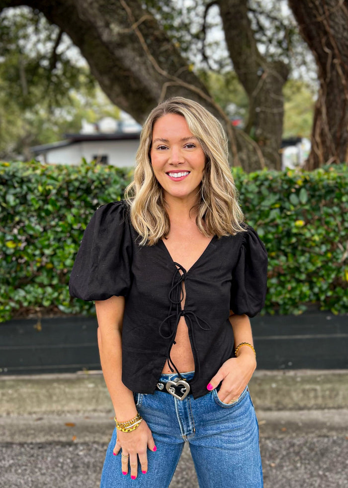 Black tie-front top with puffed short sleeves worn with blue jeans.