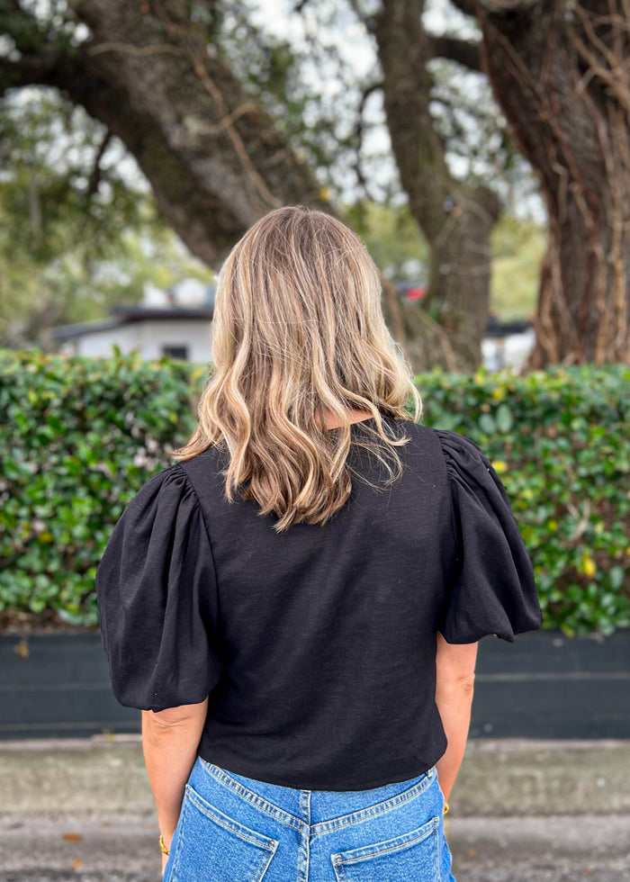 Black cotton top with puffed short sleeves, worn with blue jeans.
