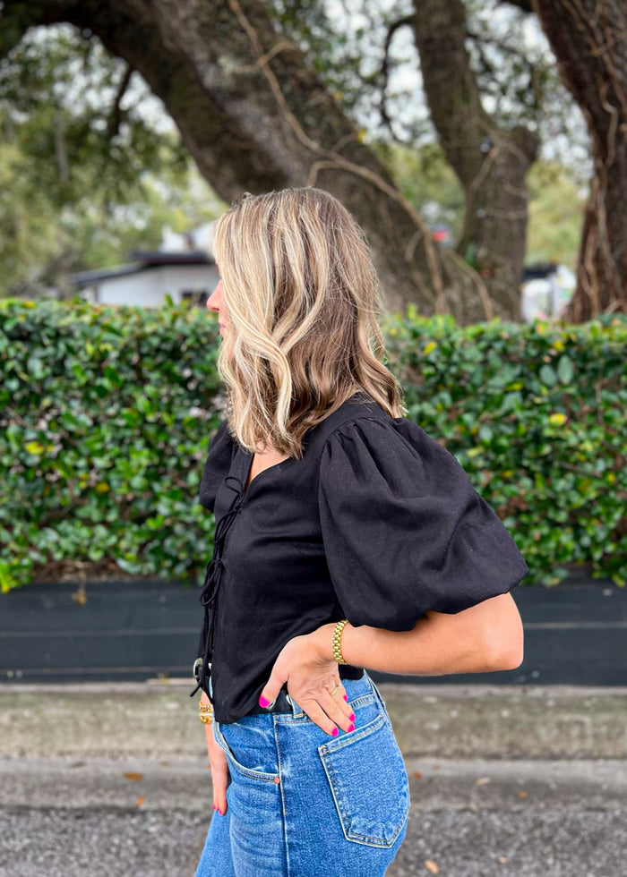 Black top with puffed short sleeves and front button placket, worn with blue jeans.