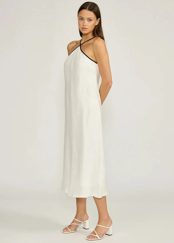 White halter midi dress with asymmetrical neckline and side pockets on model wearing white heeled sandals.