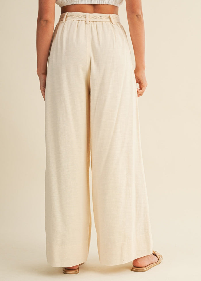 Cream pleated palazzo pants with a wide leg and woven belt, shown on a model from waist down.