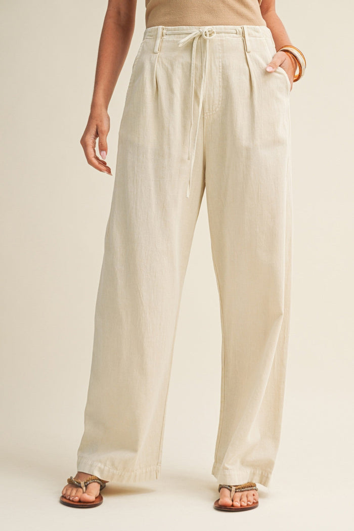 Cream linen straight-leg pants with drawstring waist and side pockets on model wearing tan top and brown sandals.