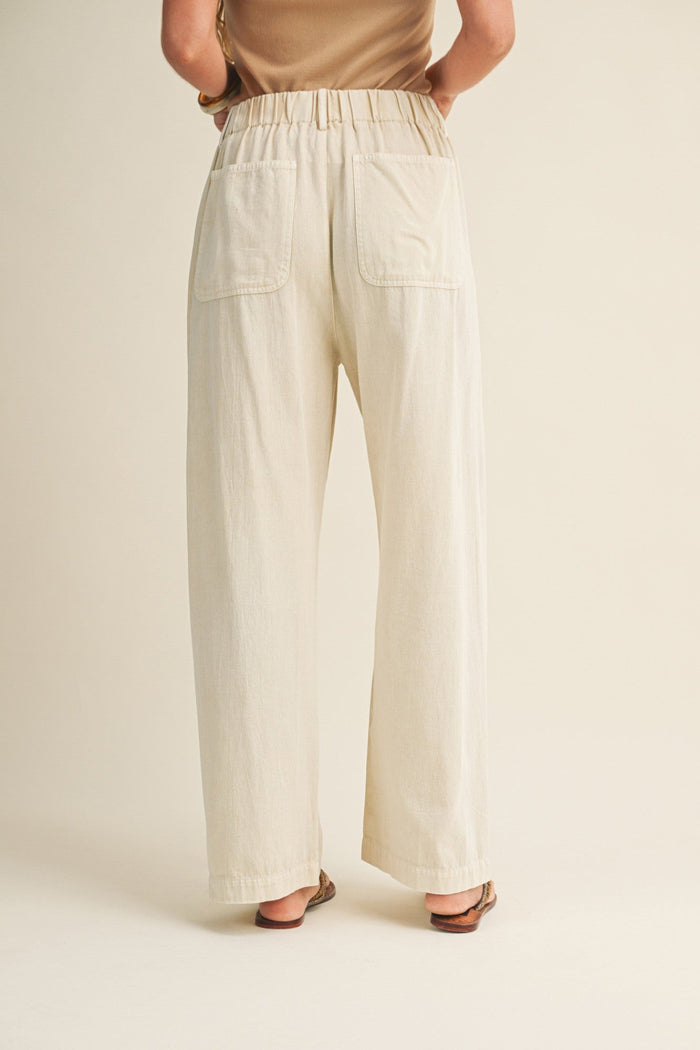 Cream straight-leg pants with elastic waistband and patch pockets, worn with tan top and brown sandals.