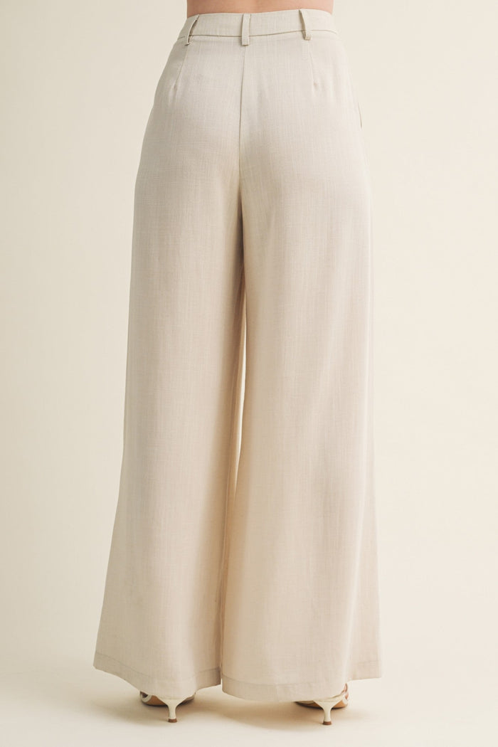 Cream-colored wide leg pants with high waist and pleated front detail, shown from back view.