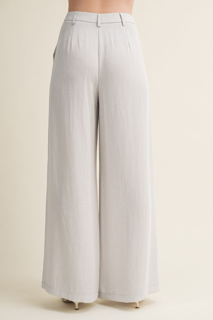 Cream wide-leg pants with high waist and pleated front detail, shown from back view on model.