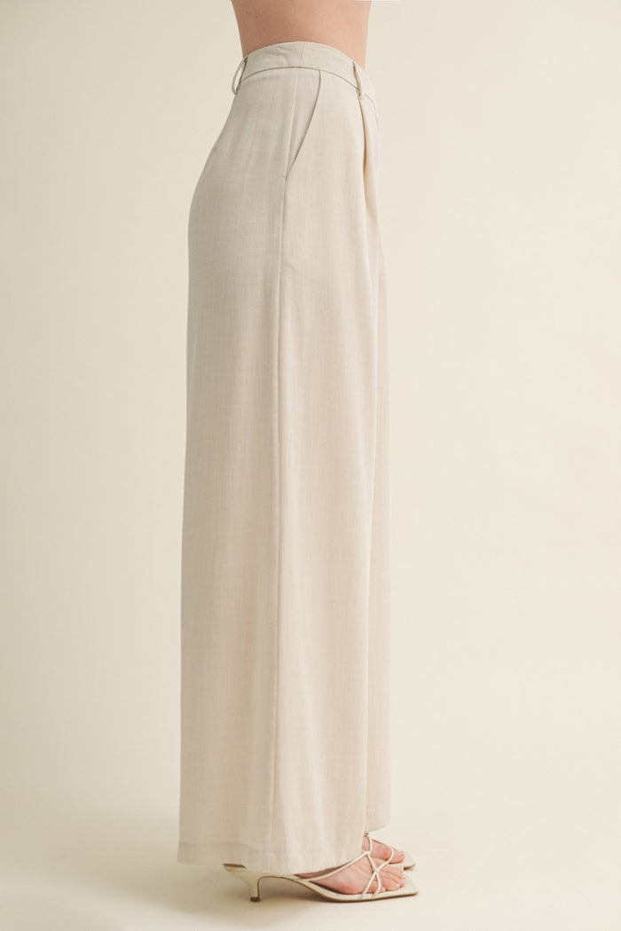 Cream wide-leg pants with high waist and pleated front, shown from side view on model wearing strappy sandals.