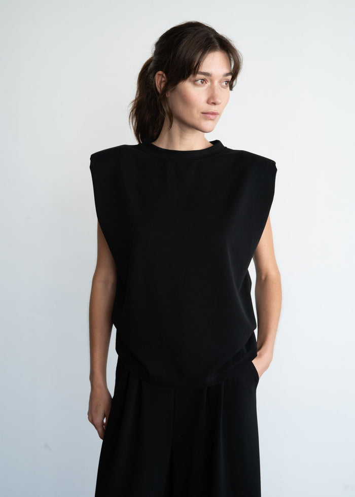 Black sleeveless top with structured shoulder pads and crew neckline on model.