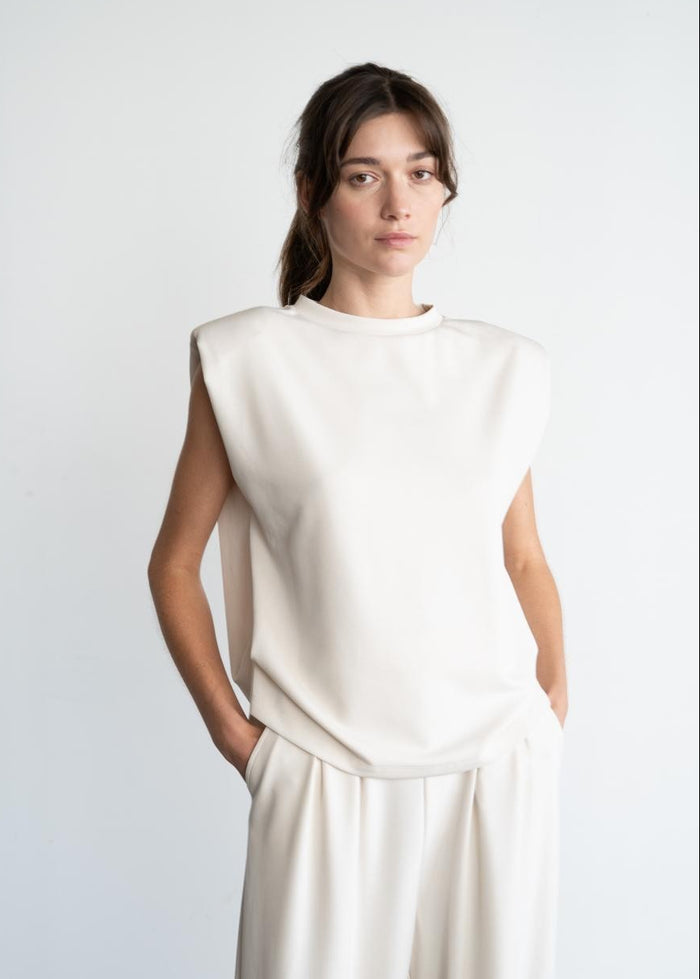 Cream sleeveless top with padded shoulders and crew neckline on model wearing matching cream pants.