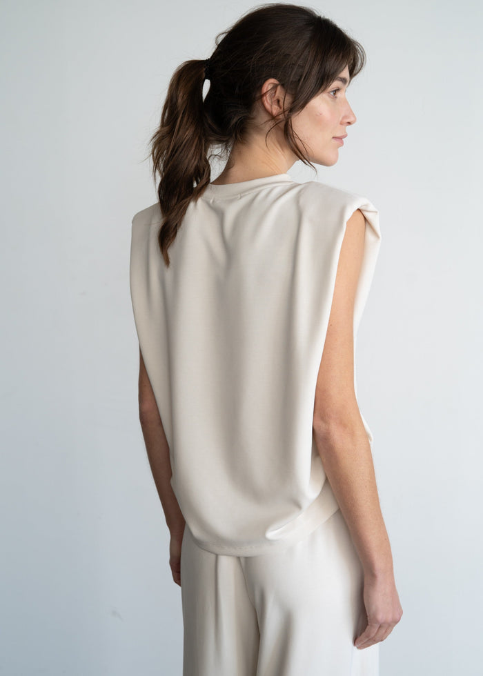 Cream sleeveless top with structured shoulder pads, shown from back on model with ponytail.