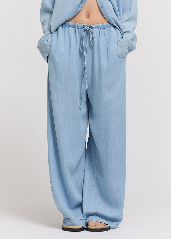 Light blue chambray pants with elastic waistband and drawstring, straight leg silhouette.