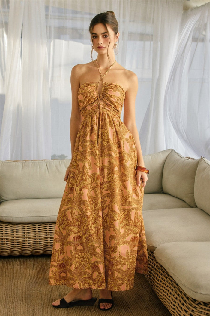 Woman wearing a gold halter maxi dress with botanical print, paired with a gold chain necklace and black sandals.