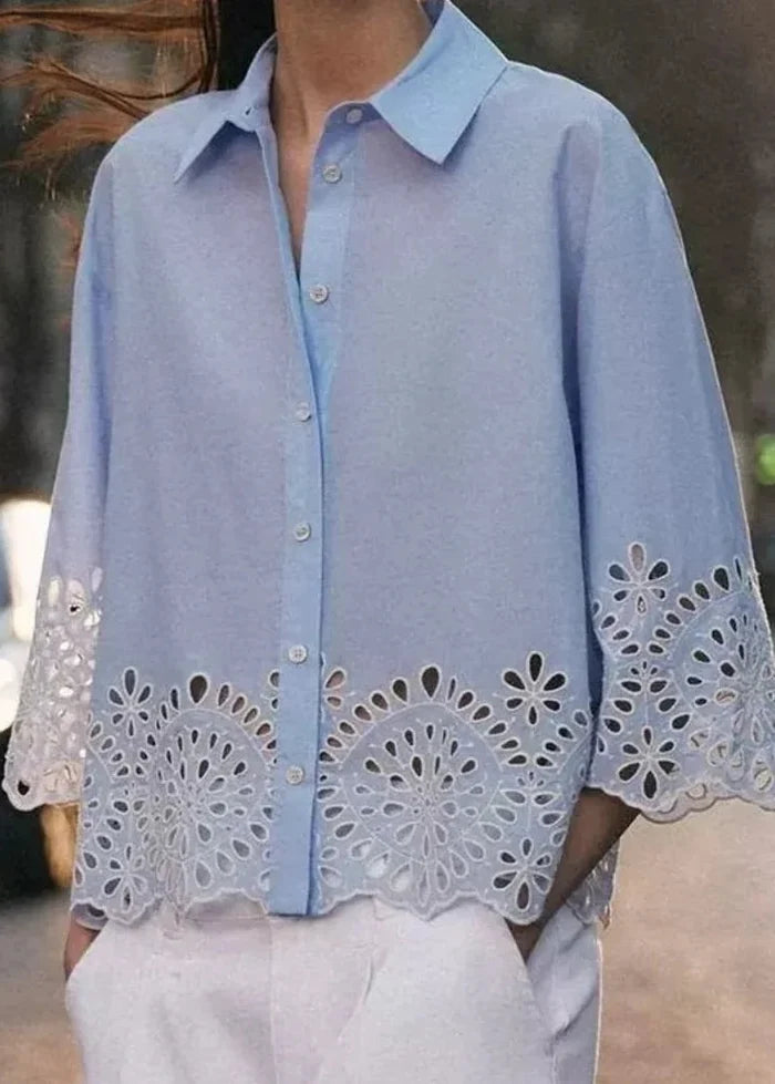 Light blue button-down top with collar and three-quarter sleeves featuring white eyelet embroidery trim at cuffs and hem.