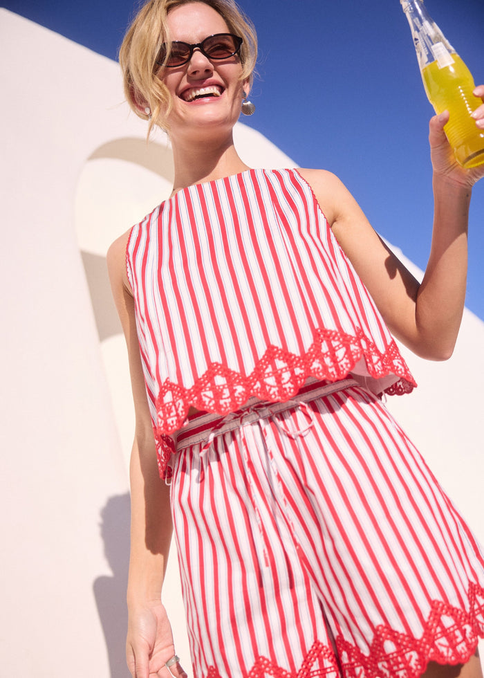 Woman in a red and white striped dress holding a drink against a bright blue sky.