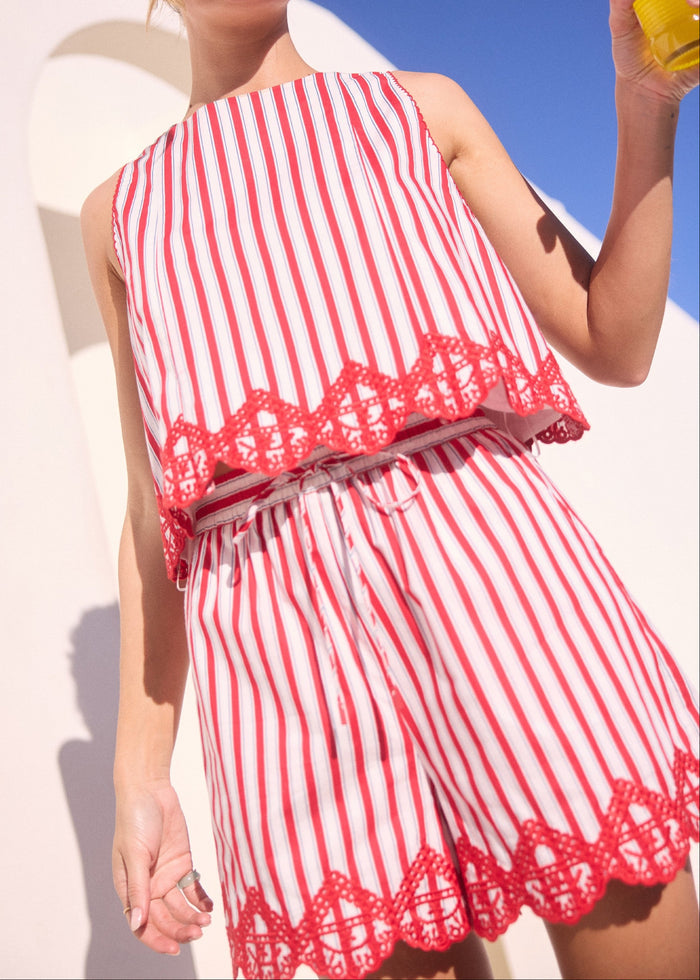 Woman in a red and white striped dress holding a drink against a bright blue sky.