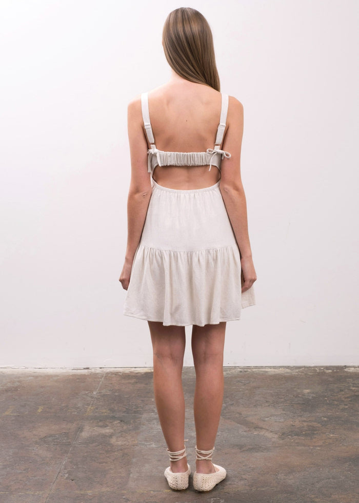 White sleeveless dress with open back, tie shoulder straps, and tiered skirt with dropped waistline.