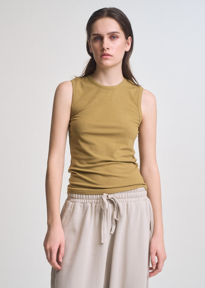 Olive-green sleeveless tank with crew neckline and wide shoulders on model wearing beige drawstring pants.