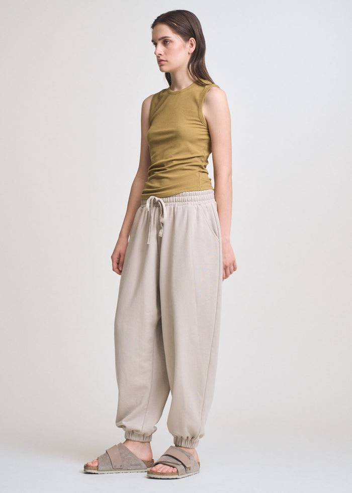 Olive sleeveless tank with wide shoulders and gathered sides, paired with cream jogger pants.