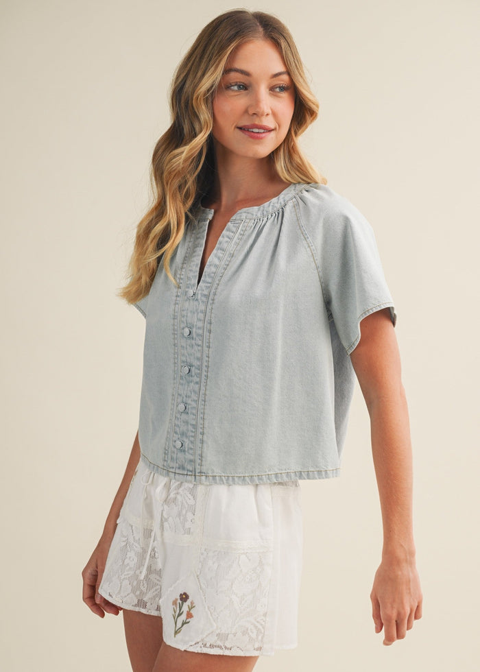 Light wash denim top with V-neckline, short sleeves, and button front closure.