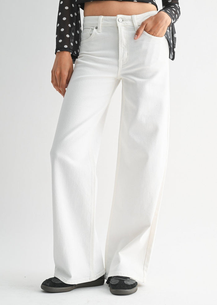 White high-rise straight leg jeans with button and zip closure, worn with black polka dot top and black slippers.