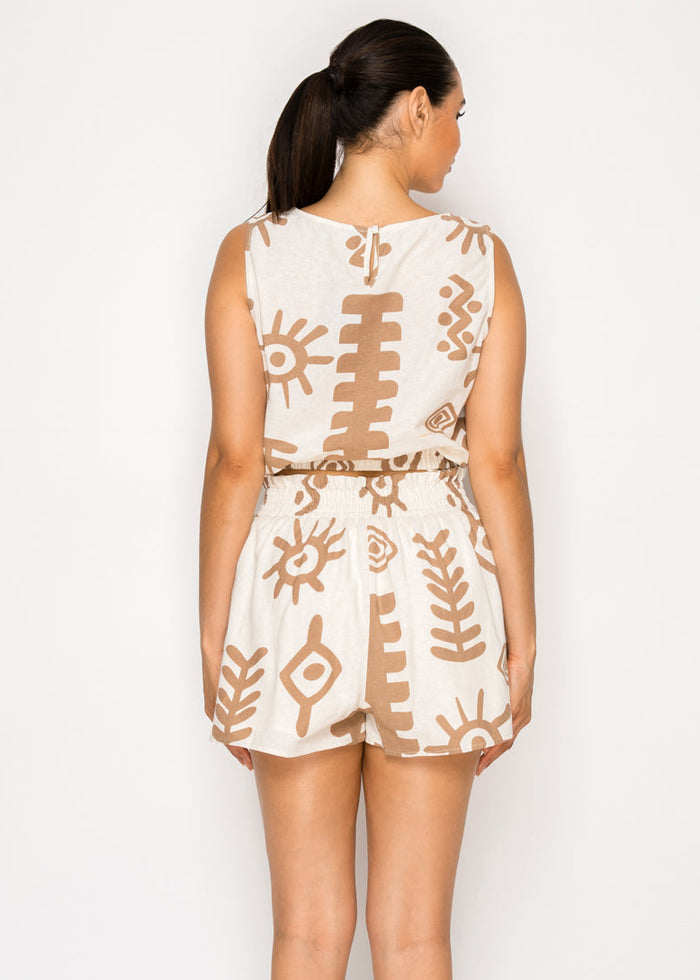 Woman wearing cream sleeveless seersucker top with tan geometric print and matching shorts, shown from behind.